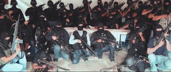 Movie still from “Cartel Land” (2015), directed by Matthew Heineman – A group of men sitting on the ground holding guns; Wide shot, High angle