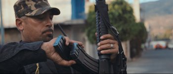 Movie still from “Cartel Land” (2015), directed by Matthew Heineman – A man holding an ar - 1 5 style rifle and a cell phone; Close Up shot, Low angle