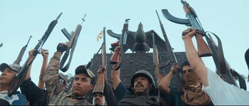 Movie still from “Cartel Land” (2015), directed by Matthew Heineman – A group of men holding guns in front of an eagle statue; Medium shot, Low angle