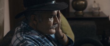 Movie still from “Cartel Land” (2015), directed by Matthew Heineman – An older man wearing a black hat sitting in a chair; Close Up shot, Over the shoulder angle