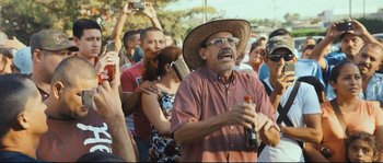Movie still from “Cartel Land” (2015), directed by Matthew Heineman – An older man holding a bottle of beer in front of a group of people; Medium shot, Over the shoulder angle