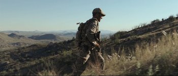 Movie still from “Cartel Land” (2015), directed by Matthew Heineman – A man walking on top of a hill with a backpack; Wide shot, Over the shoulder angle