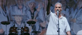Movie still from “Cartel Land” (2015), directed by Matthew Heineman – A man with a beard and a microphone in front of a painting; Medium shot, Low angle