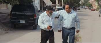 Movie still from “Cartel Land” (2015), directed by Matthew Heineman – Two men walking down the street one is holding a cell phone; Medium shot, Over the shoulder angle