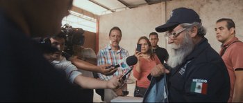 Movie still from “Cartel Land” (2015), directed by Matthew Heineman – A group of people standing in a room holding microphones; Medium shot, Over the shoulder angle