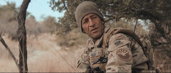 Movie still from “Cartel Land” (2015), directed by Matthew Heineman – A man in a military uniform is sitting in a field; Close Up shot, Over the shoulder angle