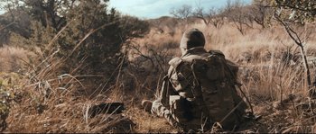 Movie still from “Cartel Land” (2015), directed by Matthew Heineman – A soldier sitting on the ground in a field; Wide shot, Low angle