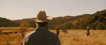 Movie still from “Casa de mi Padre” (2012), directed by Matt Piedmont – A man wearing a cowboy hat looking out at a herd of horses; Wide shot, Over the shoulder angle
