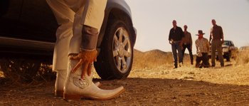 Movie still from “Casa de mi Padre” (2012), directed by Matt Piedmont – A man standing in front of a car on the side of a dirt road; Wide shot, Low angle