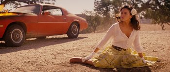 Movie still from “Casa de mi Padre” (2012), directed by Matt Piedmont – A woman sitting on the ground in front of a red car; Wide shot, Low angle