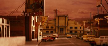 Movie still from “Casa de mi Padre” (2012), directed by Matt Piedmont – A street scene with a building and cars on the road; Extreme Wide shot, High angle