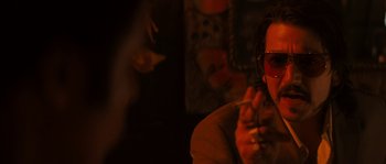 Movie still from “Casa de mi Padre” (2012), directed by Matt Piedmont – A man with sunglasses is smoking a cigarette in a dark room; Close Up shot, Over the shoulder angle