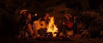 Movie still from “Casa de mi Padre” (2012), directed by Matt Piedmont – A group of people sitting around a fire with guitars; Wide shot, High angle
