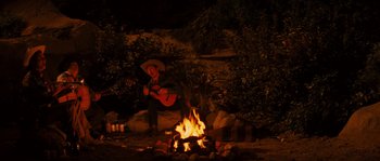 Movie still from “Casa de mi Padre” (2012), directed by Matt Piedmont – A man in a cowboy hat playing a guitar near a campfire; Wide shot, Over the shoulder angle