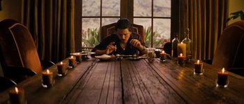 Movie still from “Casa de mi Padre” (2012), directed by Matt Piedmont – A man sitting at a wooden table eating food; Medium shot, Low angle