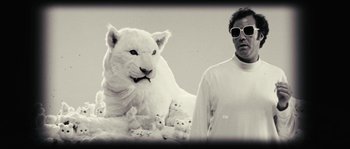 Movie still from “Casa de mi Padre” (2012), directed by Matt Piedmont – A man standing in front of a stuffed animal tiger; Medium shot, Low angle