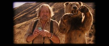 An older man holding a cell phone next to a bear