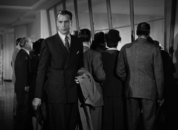 Movie still from “Casanova Brown” (1944), directed by Sam Wood – Black and white photograph of a man in a suit and tie in front of a group of people; Medium shot, Low angle