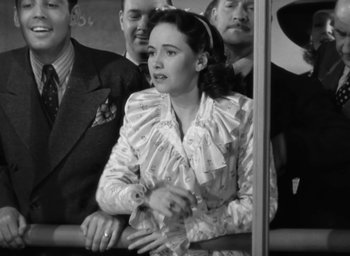 Movie still from “Casanova Brown” (1944), directed by Sam Wood – An old photo of a woman holding a bottle in a crowd; Medium shot, High angle