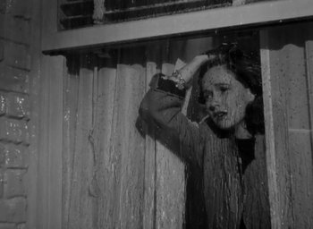 Movie still from “Casanova Brown” (1944), directed by Sam Wood – A young woman smoking a cigarette while standing in the rain; Medium shot, Low angle