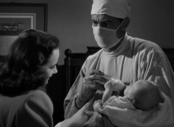 Movie still from “Casanova Brown” (1944), directed by Sam Wood – An old black and white photo of a doctor holding a baby; Medium shot, Low angle