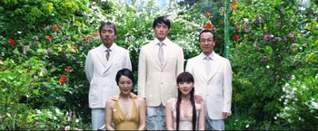 Movie still from “Casshern” (2004), directed by Kazuaki Kiriya – A group of people standing next to each other in front of flowers; Wide shot, Low angle