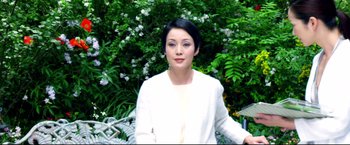 Movie still from “Casshern” (2004), directed by Kazuaki Kiriya – A woman wearing a white jacket standing in front of some bushes; Medium shot, Low angle
