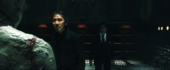 Movie still from “Casshern” (2004), directed by Kazuaki Kiriya – Two men in black suits standing next to each other in a dark room; Medium shot, Over the shoulder angle