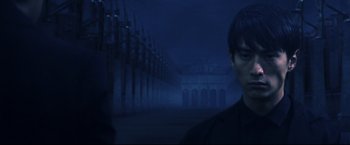 Movie still from “Casshern” (2004), directed by Kazuaki Kiriya – A man standing in front of a building at night; Medium shot, Over the shoulder angle