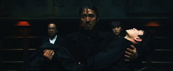 Movie still from “Casshern” (2004), directed by Kazuaki Kiriya – A group of people standing next to each other in a dark room; Medium shot, Low angle