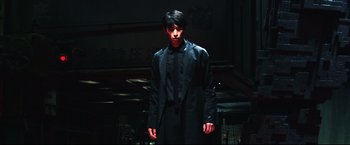 Movie still from “Casshern” (2004), directed by Kazuaki Kiriya – A young man in a black suit standing in a dark room; Medium shot, Low angle