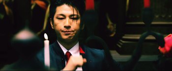 Movie still from “Casshern” (2004), directed by Kazuaki Kiriya – A man in a suit and red tie holding a microphone; Extreme Close Up shot, Low angle