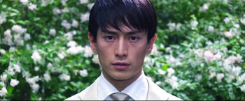 Movie still from “Casshern” (2004), directed by Kazuaki Kiriya – A man in a suit and tie in front of a bush; Close Up shot, Low angle
