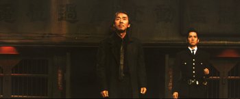Movie still from “Casshern” (2004), directed by Kazuaki Kiriya – A man wearing a black coat and a black tie; Medium shot, Low angle