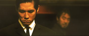 Movie still from “Casshern” (2004), directed by Kazuaki Kiriya – A man wearing a suit and tie standing next to another man wearing a suit and tie; Close Up shot, Low angle