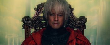 Movie still from “Casshern” (2004), directed by Kazuaki Kiriya – A man sitting in a chair wearing a red jacket; Close Up shot, Low angle