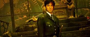Movie still from “Casshern” (2004), directed by Kazuaki Kiriya – A man in a suit holding a sword in front of a wall; Medium shot, Low angle