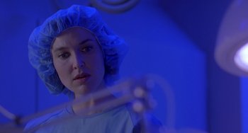 Movie still from “The Craft” (1996), directed by Andrew Fleming – A woman in a surgical gown and a surgical cap is looking at the camera; Close Up shot, Over the shoulder angle