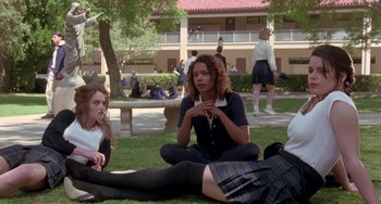 Movie still from “The Craft” (1996), directed by Andrew Fleming – A group of people sitting on the grass in front of a building; Medium shot, High angle