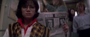 Movie still from “Casualties of War” (1989), directed by Brian De Palma – A woman in glasses is holding up a newspaper; Medium shot, Over the shoulder angle