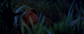 Movie still from “Casualties of War” (1989), directed by Brian De Palma – A man wearing a hat is laying in the grass at night; Close Up shot, Low angle