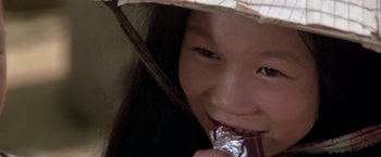 Movie still from “Casualties of War” (1989), directed by Brian De Palma – A young girl is eating a chocolate bar while wearing a hat; Extreme Close Up shot, High angle