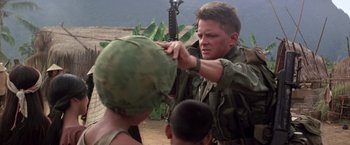 Movie still from “Casualties of War” (1989), directed by Brian De Palma – A man in fatigues is holding a rifle and putting on a hat; Close Up shot, Over the shoulder angle