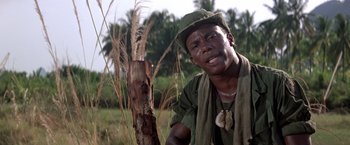 Movie still from “Casualties of War” (1989), directed by Brian De Palma – A man wearing a hat and a scarf leaning against a tree; Close Up shot, Low angle