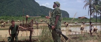 Movie still from “Casualties of War” (1989), directed by Brian De Palma – A man holding a rifle in his hand; Wide shot, Over the shoulder angle