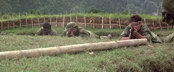 Movie still from “Casualties of War” (1989), directed by Brian De Palma – A group of men laying in the grass next to a log fence; Wide shot, High angle