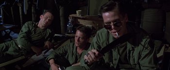 Movie still from “Casualties of War” (1989), directed by Brian De Palma – A group of men sitting next to each other holding guns; Medium shot, Low angle