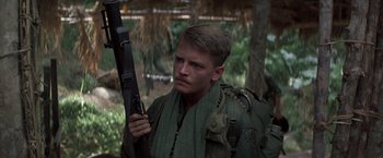 Movie still from “Casualties of War” (1989), directed by Brian De Palma – A man holding a rifle while wearing a green shirt; Close Up shot, Low angle