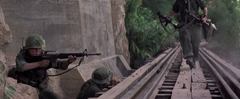 Movie still from “Casualties of War” (1989), directed by Brian De Palma – A man with a rifle is sitting on a ledge; Wide shot, Low angle