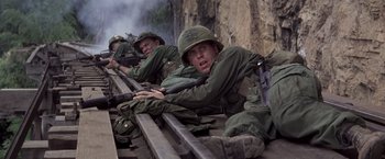 Movie still from “Casualties of War” (1989), directed by Brian De Palma – A group of men in green fatigues are sitting on a rail; Medium shot, Low angle